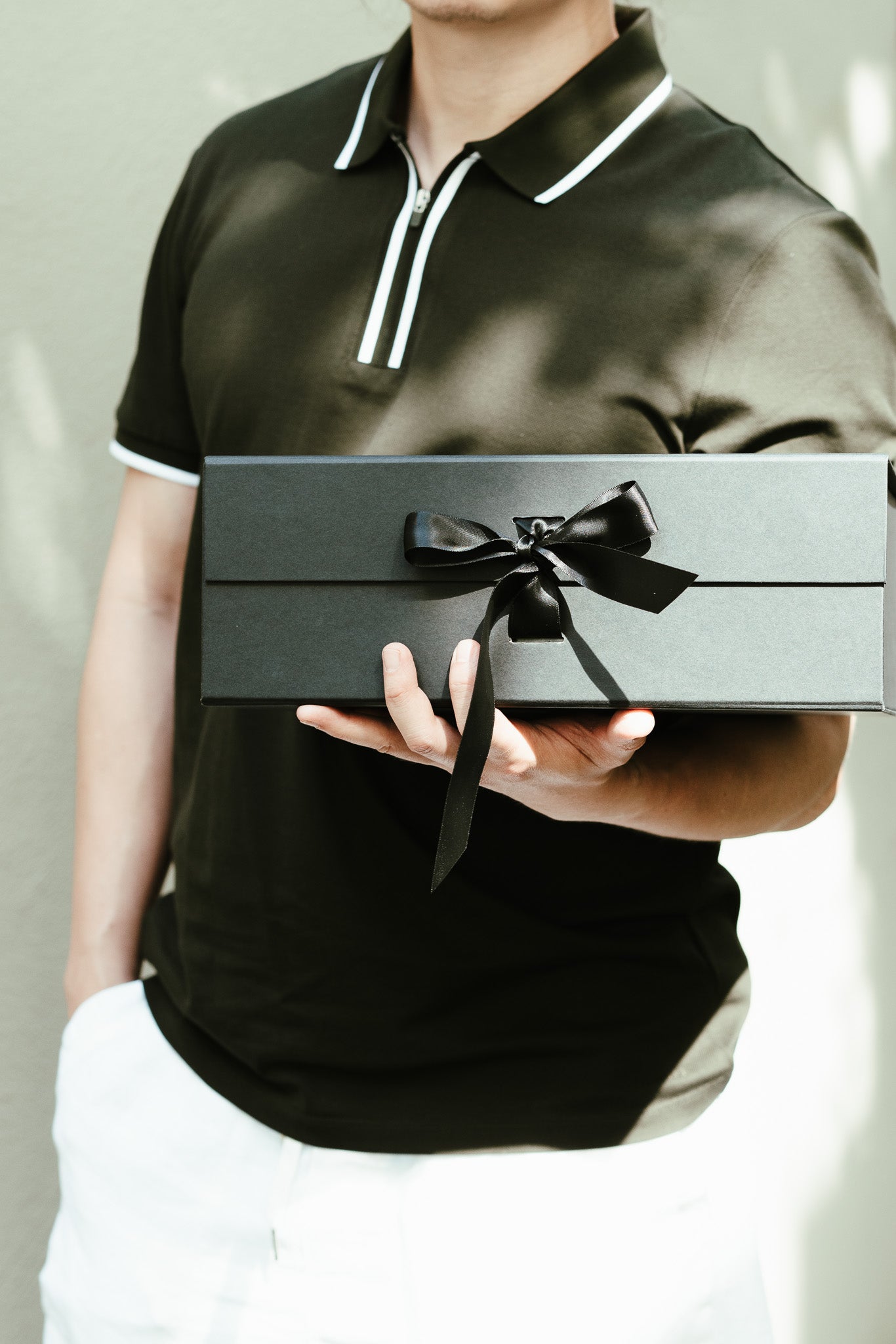Person holding a black gift box with a bow against a neutral background