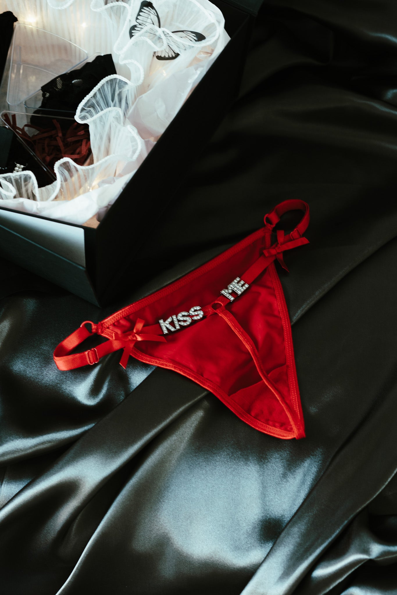 Red thong with 'Kiss Me' text on a black satin surface